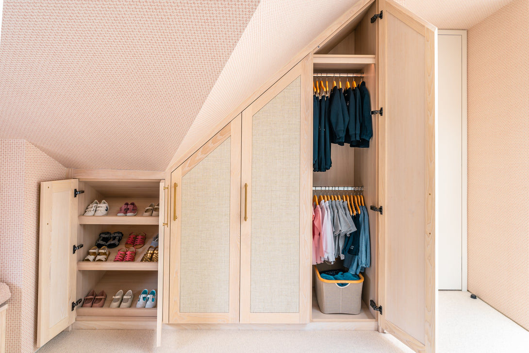 Bespoke angled wardrobes fitted under a sloping ceiling, open to show custom shoe shelving and double-height hanging rails.