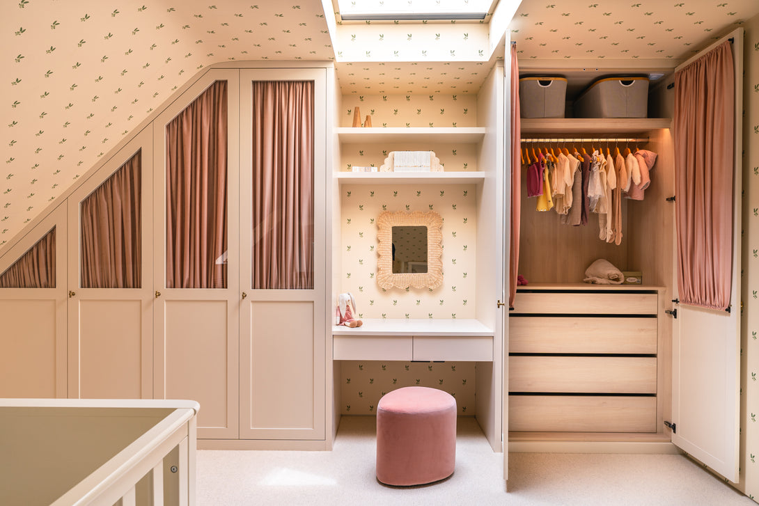 A view combining the central dressing table area with a wicker mirror and floating shelves, and an open baby wardrobe with clothes and drawers, all part of the custom nursery furniture.
