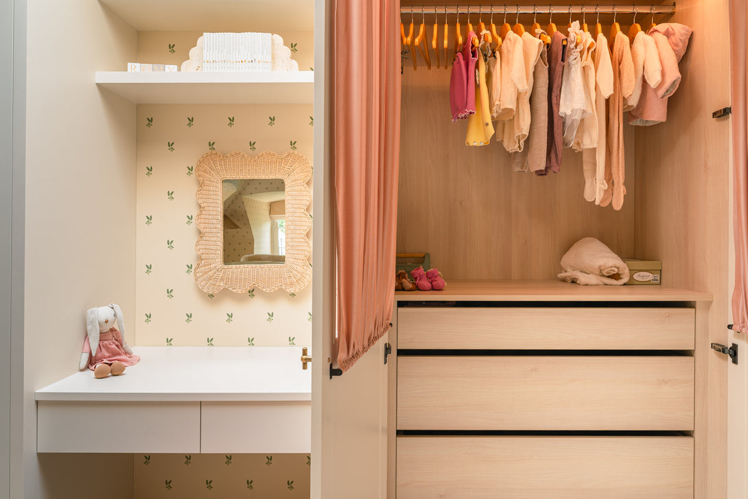 A close-up inside the baby's custom wardrobe, showing tiny clothes on hangers, a shelf with baby shoes and toys, and a soft pink curtain.