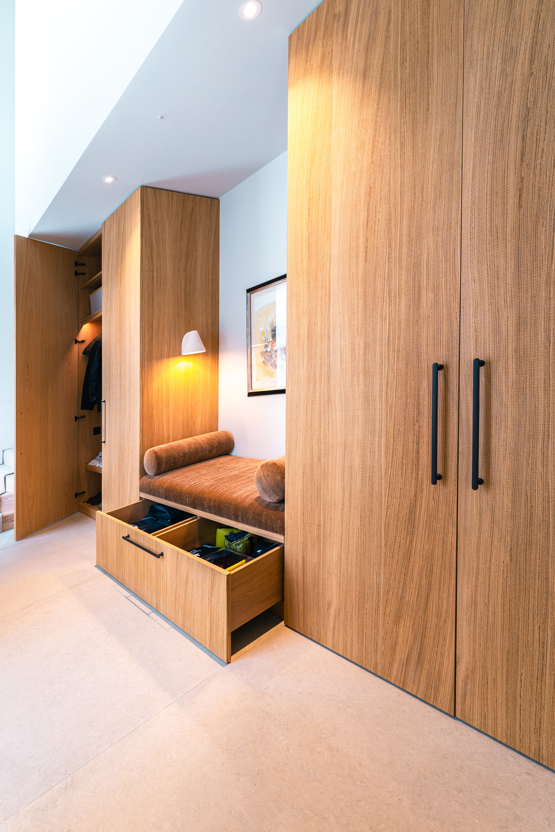 The custom oak bench seat with its upholstered cushion, showing a large storage drawer pulled open to reveal its contents. A wardrobe is visible to the side.