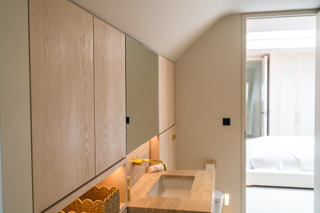 A side profile of the bespoke, handleless oak cabinetry and integrated mirror, showing the warm tones and seamless design next to the stone vanity.