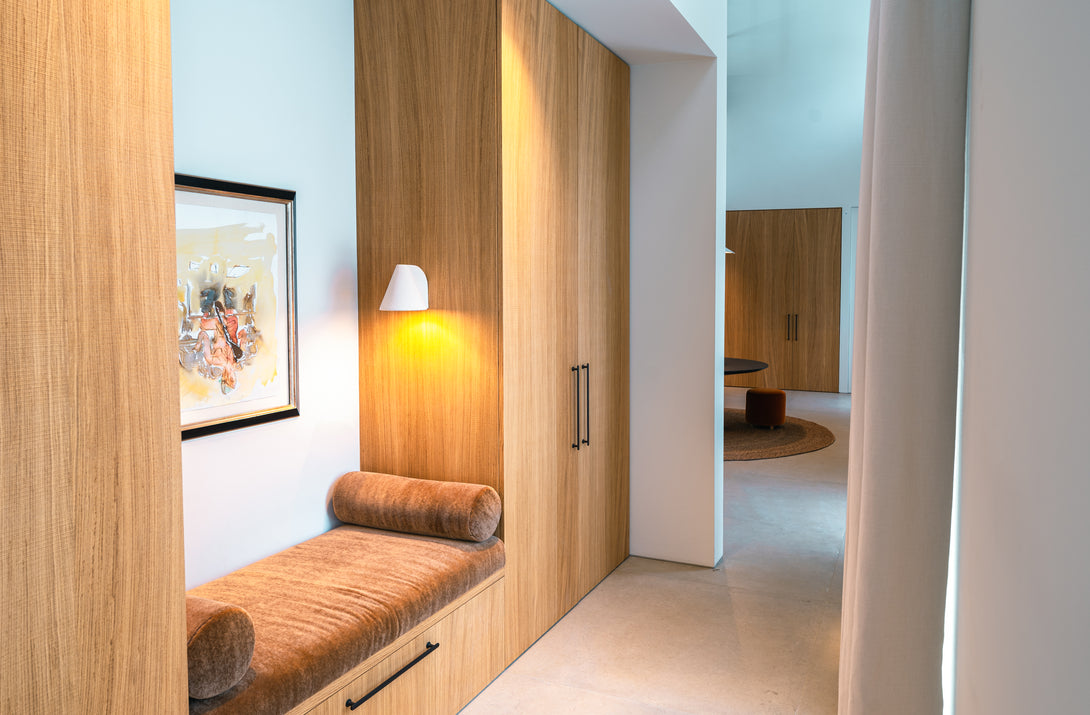 An angled view of the inviting, custom-built oak bench seat, illuminated by a modern wall sconce and positioned within a bespoke storage wall.