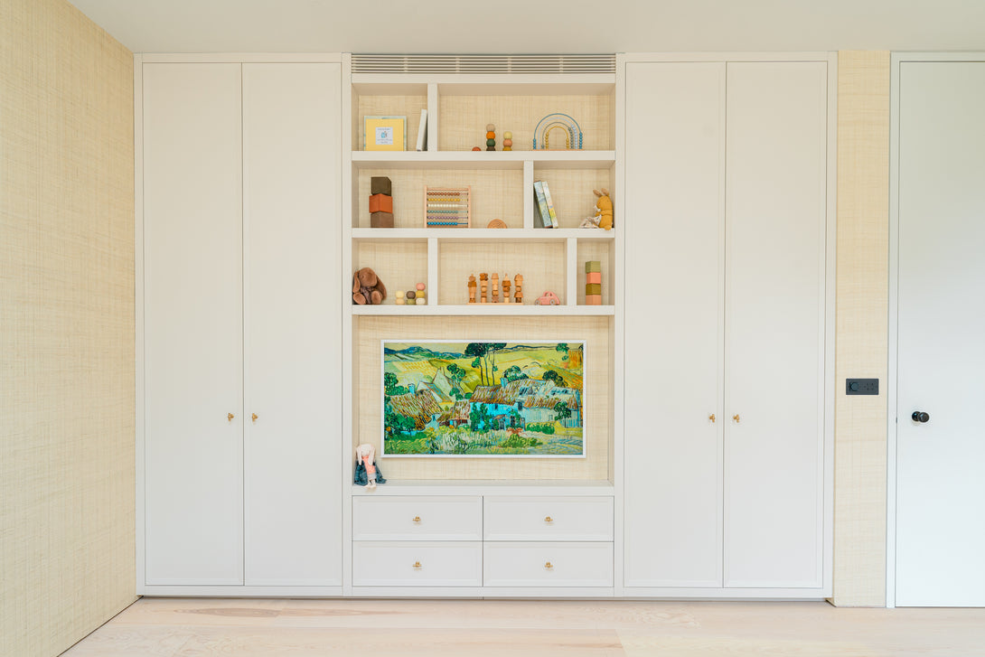 The bespoke playroom unit by Drew Furniture with all doors closed, showing a seamless, off-white facade with a central nook displaying art and toys above a bank of drawers.