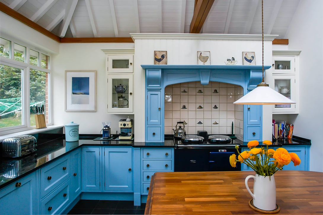A detailed view of the blue hand-painted kitchen cabinets and the ornate mantelpiece framing the range cooker and tiled splashback.