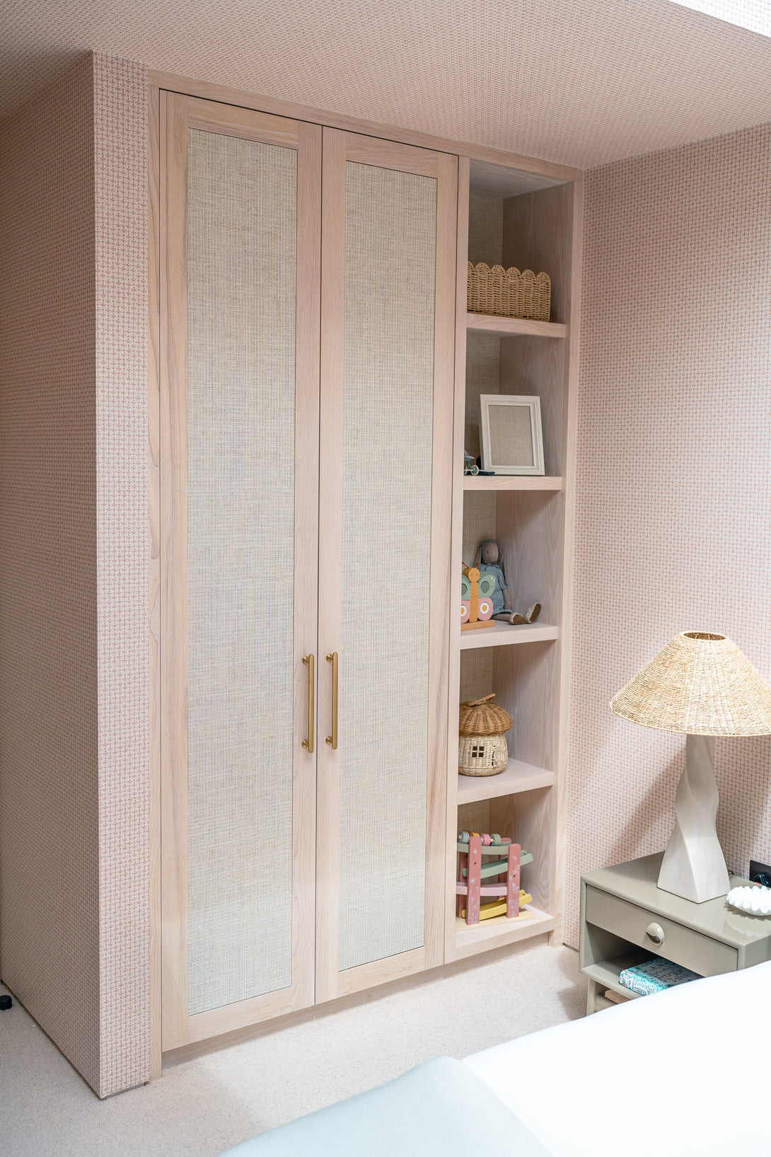 A custom light oak wardrobe with rattan panel doors and an integrated open shelving unit for displaying toys and books.