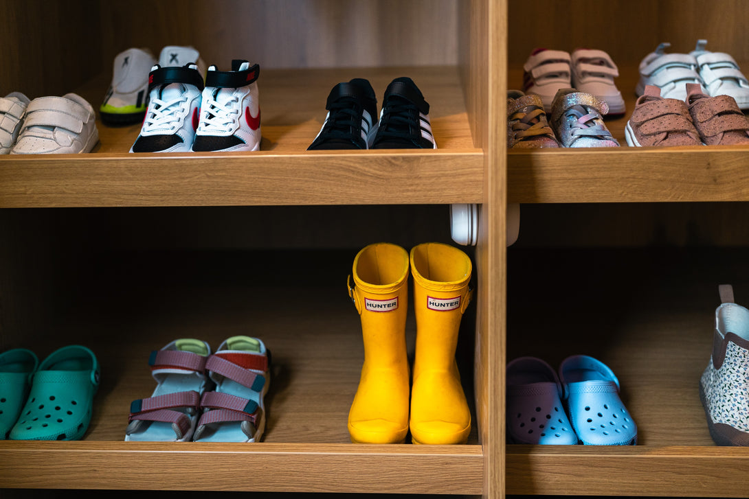 A close-up detail shot of bespoke oak shelves neatly organised with a colourful collection of children's shoes, trainers, and wellington boots.