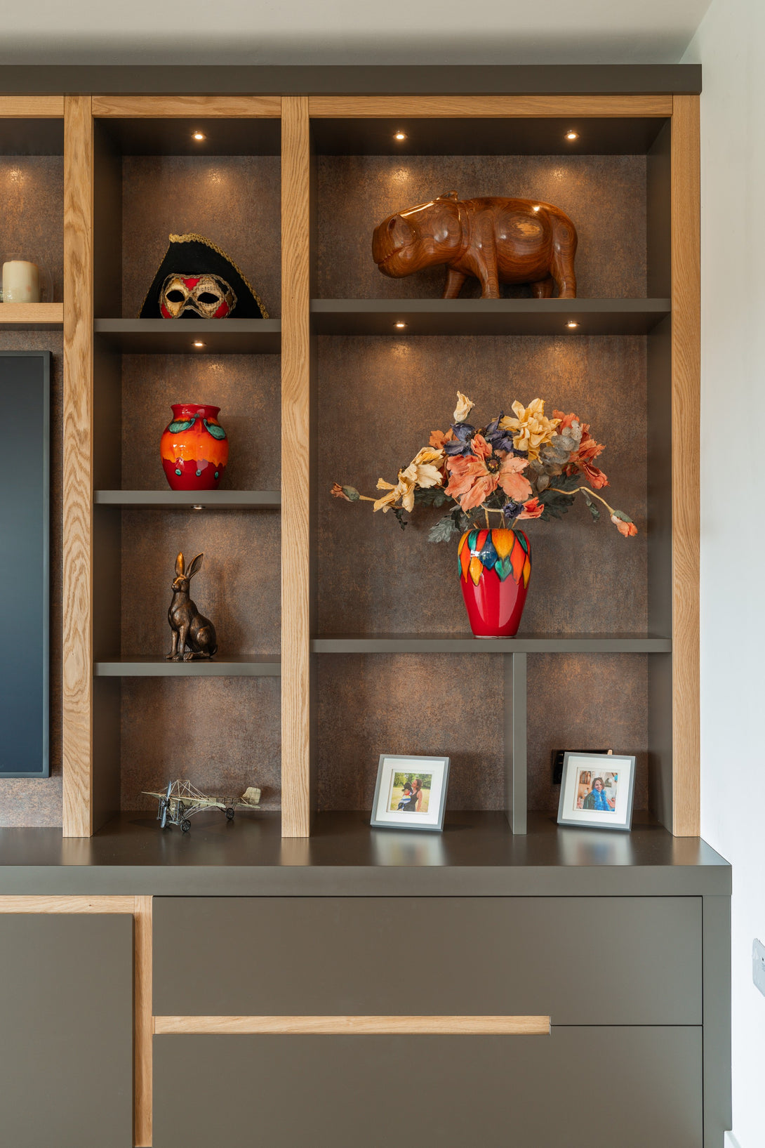 A close-up of the illuminated display shelving, showing decorative items like a vase and ornaments, highlighting the textured backing and oak frame.