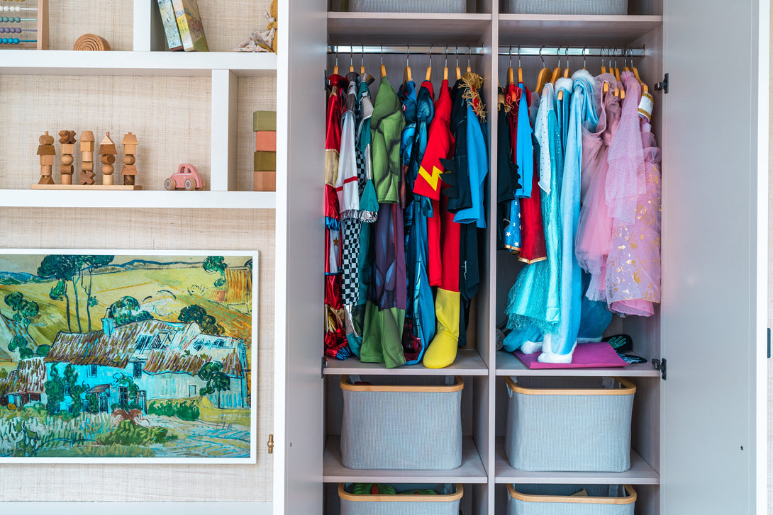 A close-up of the open dress-up wardrobe section, showing colourful costumes hanging on a rail above shelves with fabric storage baskets.