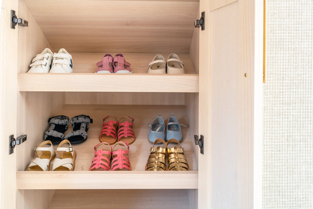 A close-up of the bespoke light oak shelves inside a shoe cupboard, neatly filled with a collection of children's shoes.