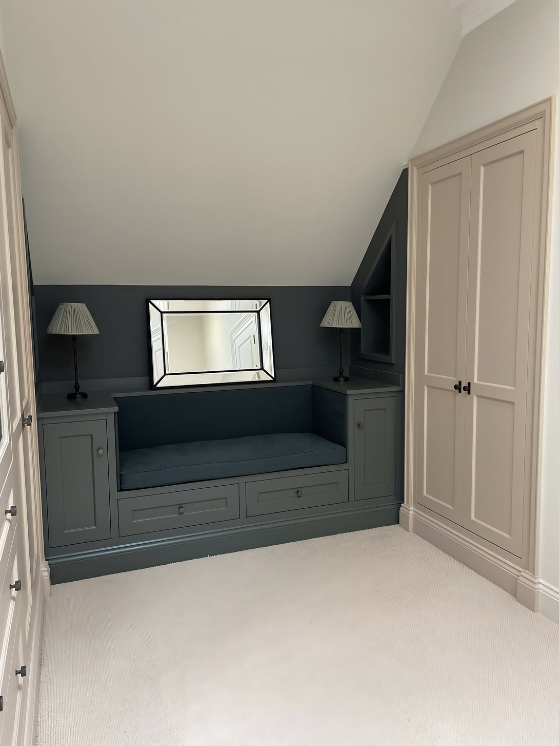 Symmetrical view of the custom-built window seat, painted dark green with an upholstered cushion, perfectly fitted between two angled wardrobes under the eaves.