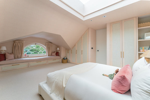 A wide view of the daughter's bedroom showing the bed, the bespoke angled wardrobes, and the large window seat, creating a cohesive and serene space.