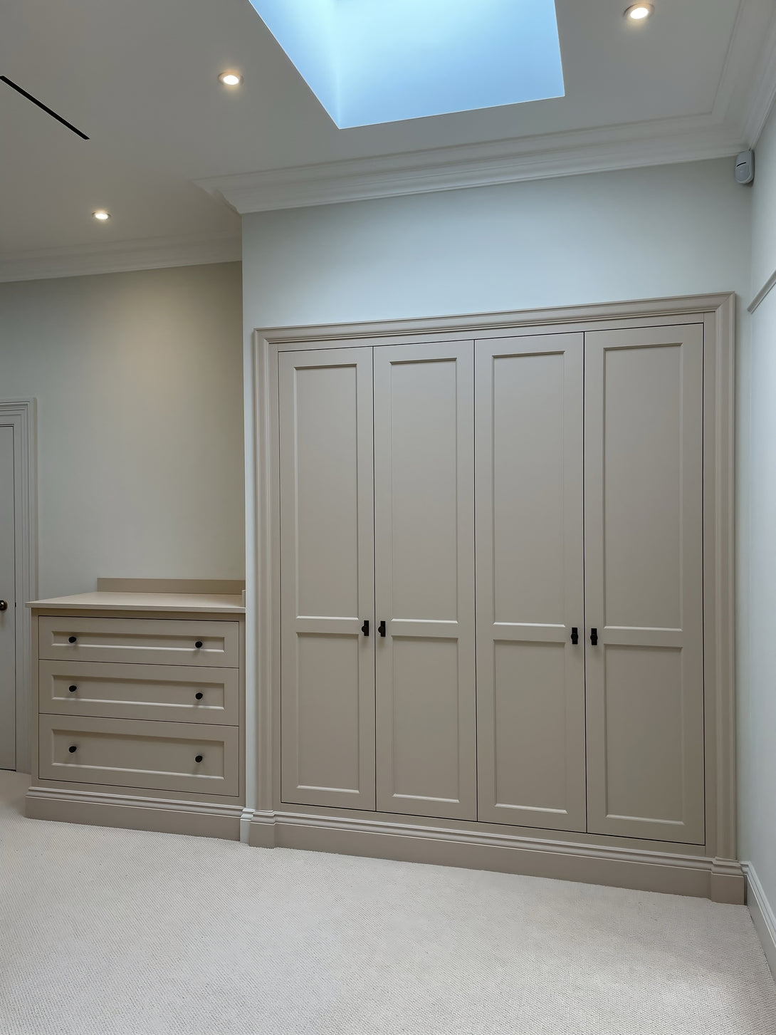 A bespoke four-door shaker wardrobe and a matching three-drawer chest of drawers, both hand-painted in a soft neutral colour with dark handles.