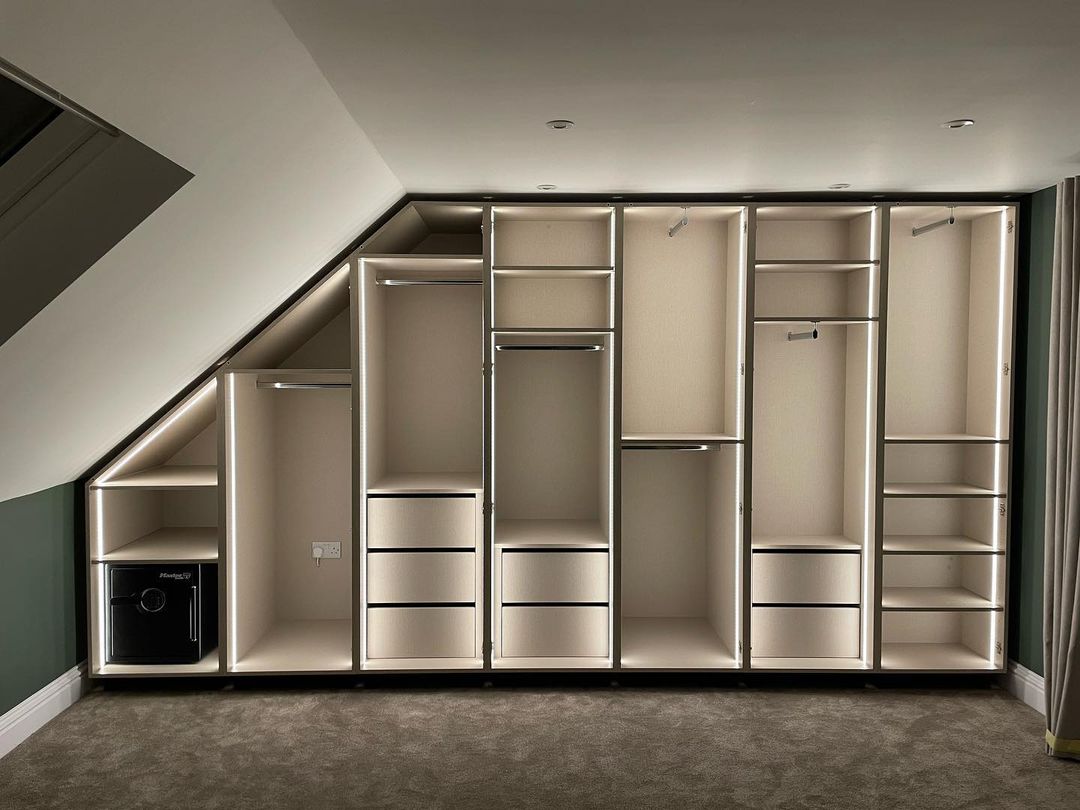 The complete interior of the bespoke loft wardrobes revealed, showcasing the custom layout of hanging rails, drawers, shelving, and integrated vertical LED lighting.