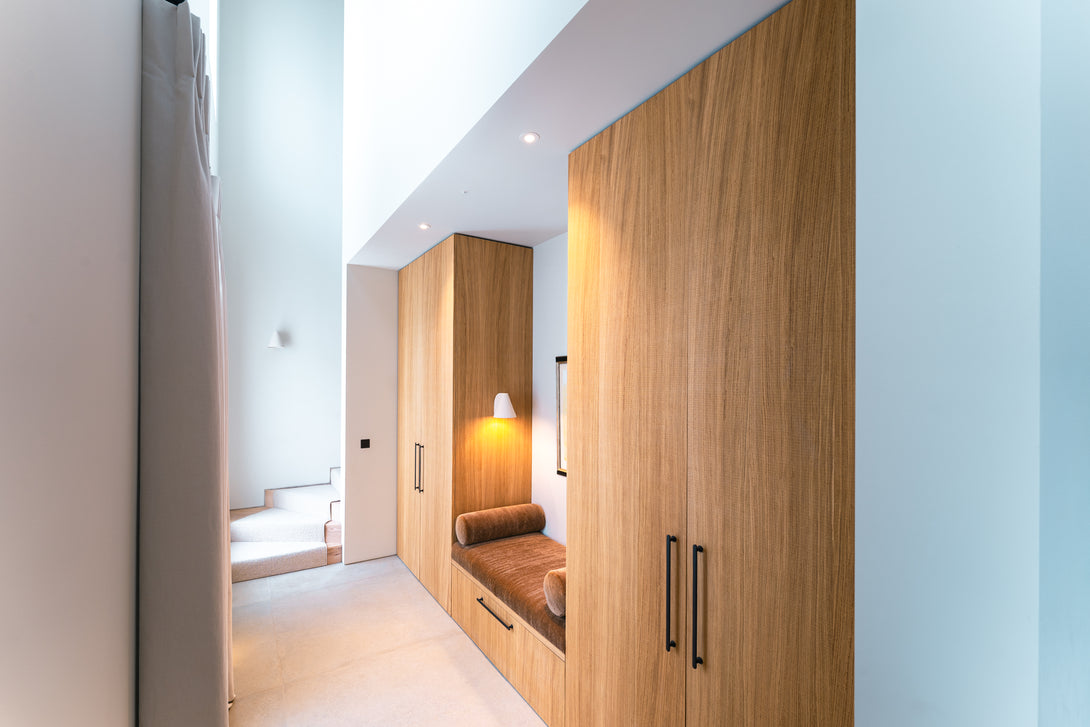 A long view of the bespoke oak boot room furniture, featuring an upholstered bench seat with storage drawers nestled beside tall oak wardrobes.