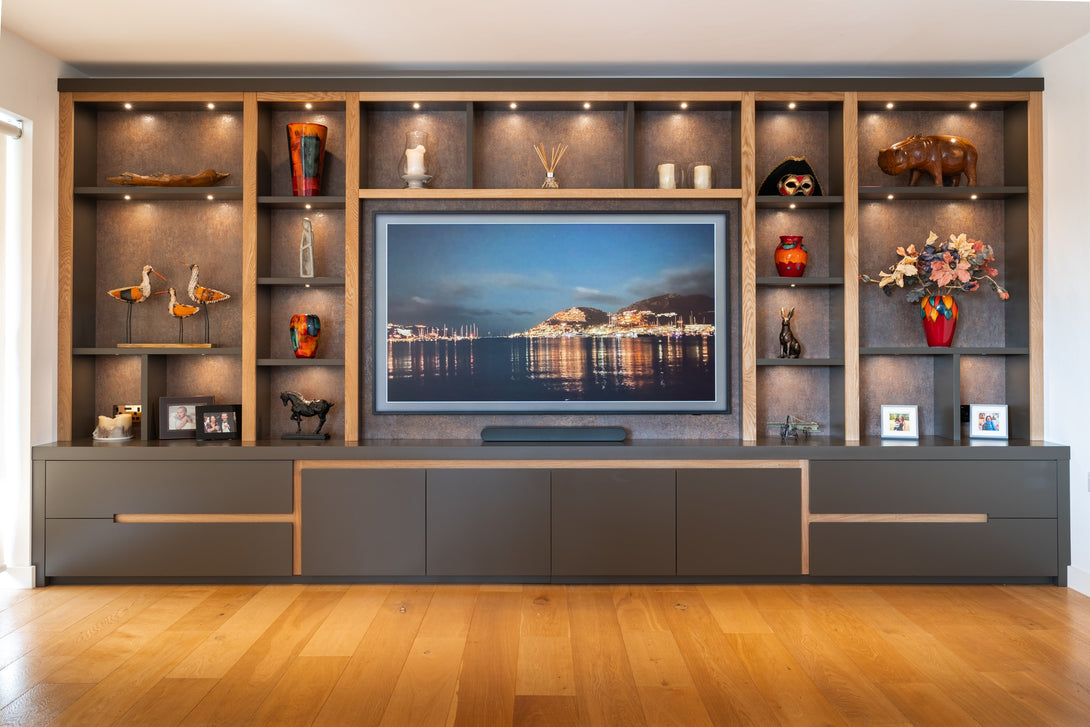 A full view of the bespoke lounge media wall by Drew Furniture, featuring illuminated shelving, a central TV, and matte grey cabinetry with oak accents.