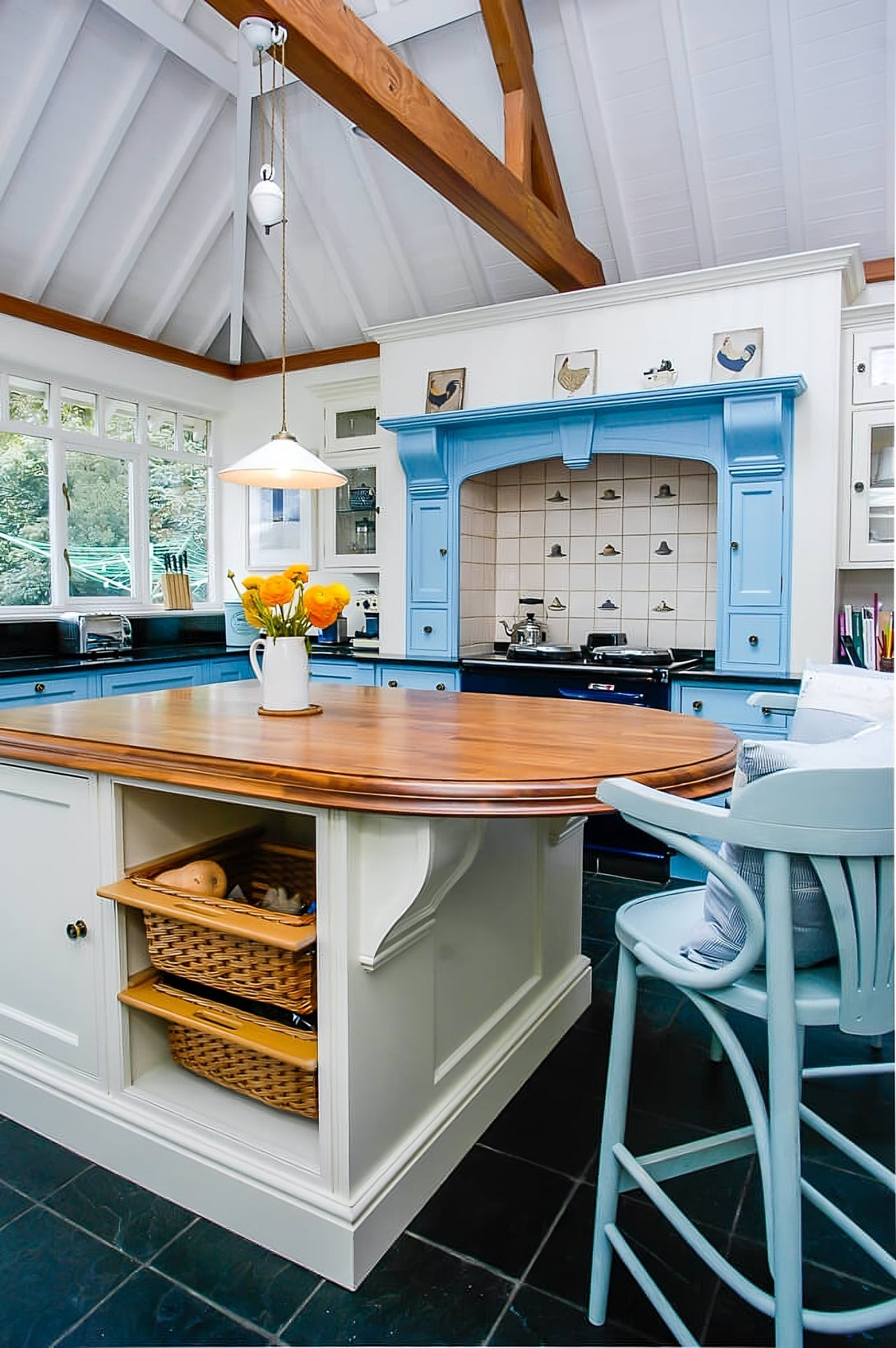 The cream-painted kitchen island showing its solid wood top and integrated storage shelves with two large wicker baskets for vegetables.