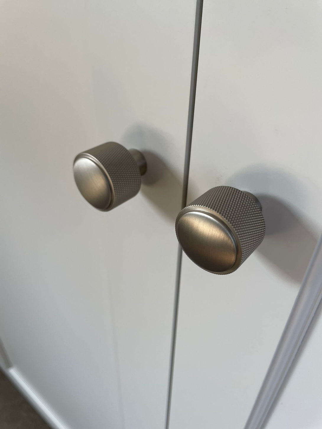 A close-up detail shot of two contemporary, knurled metal knobs on light grey, shaker-style wardrobe doors, highlighting the modern hardware.
