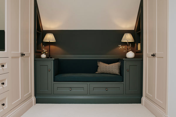 A detailed front view of the bespoke dark green window seat, featuring drawers, side cupboards, and warm lighting from the table lamps.