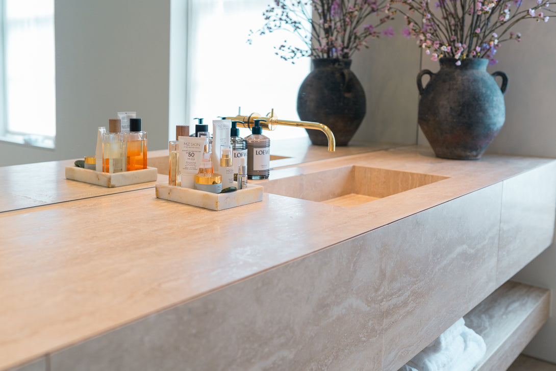 Close-up detail of an integrated sink carved from travertine stone on the bespoke vanity unit, showing the beautiful texture and a modern gold tap.