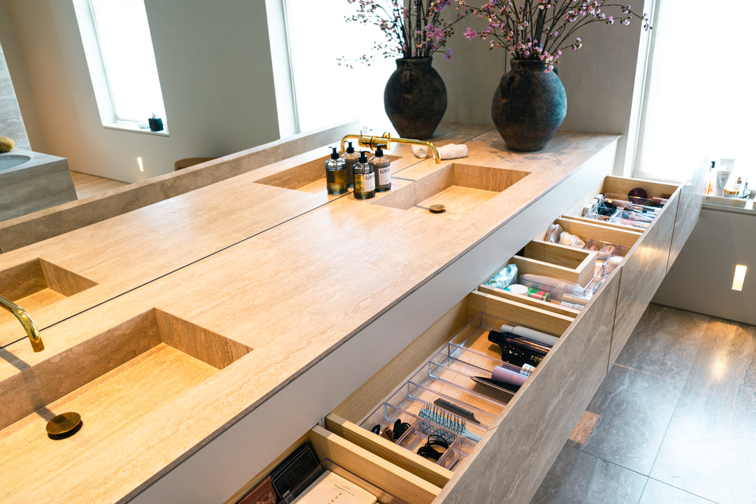 Angled view of the bespoke travertine vanity unit, with drawers open to show the custom solid oak interior organisers filled with toiletries and makeup.