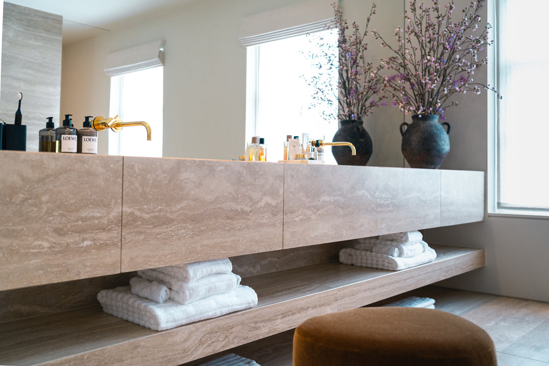 Side profile of the floating travertine vanity and matching shelf in a luxury Master Ensuite, highlighting the minimalist design and seamless stone finish by Drew Furniture.
