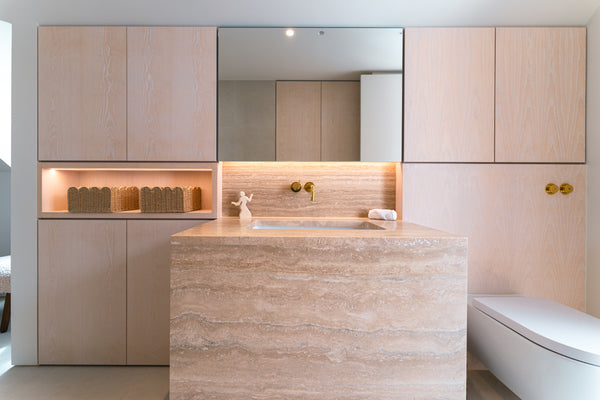  A front view of the Daughter's Ensuite Bathroom, showing the bespoke light oak cabinetry closed, framing a central mirror and a freestanding travertine stone vanity.