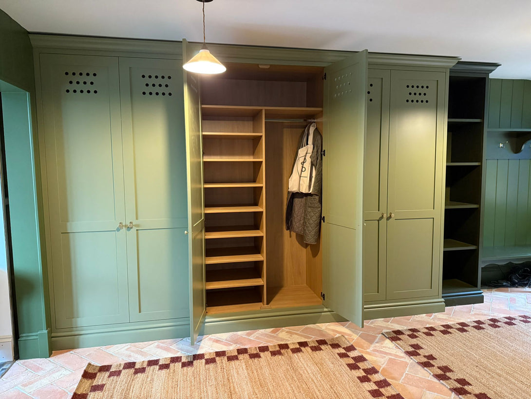 An open view of an olive green boot room cabinet, revealing a custom natural oak interior with a hanging rail and adjustable shelving for organised storage.