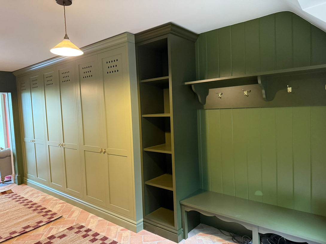 A detailed view of the integrated boot room bench, coat hooks, and open shelving, hand-painted in a dark green to contrast with the main olive cabinets.