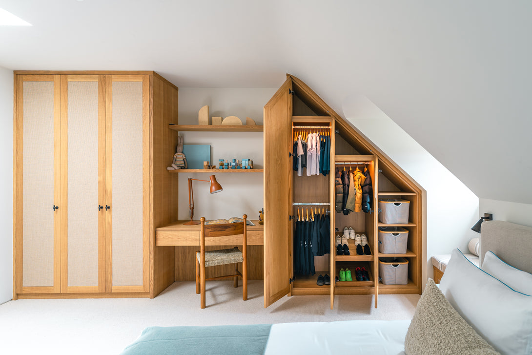 An angled view of the son's bedroom showing bespoke oak and rattan fitted wardrobes under a sloping ceiling, with one wardrobe open to reveal interior storage.