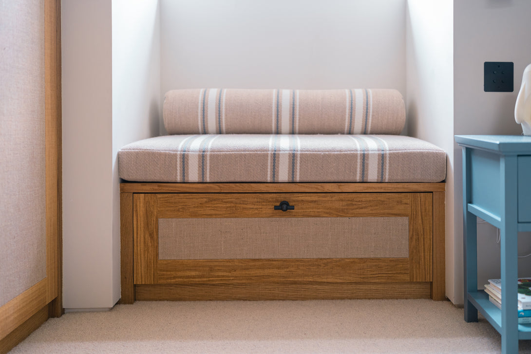 A bespoke oak window seat with a woven rattan panel drawer and striped upholstered cushion, designed for a son's bedroom.