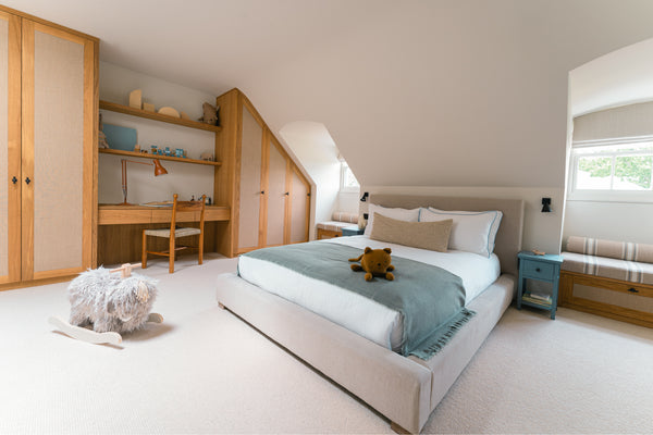 A wide view of the son's bedroom, showcasing bespoke oak and rattan fitted wardrobes, an integrated desk, a window seat, and a large bed.