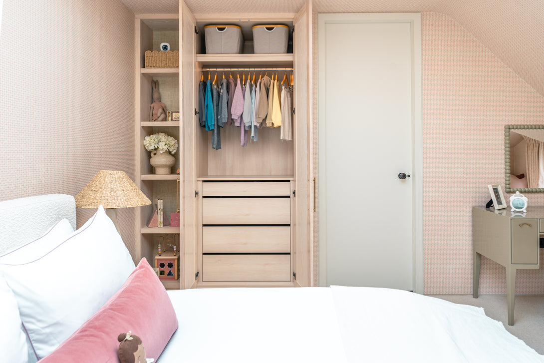 An open bespoke wardrobe in the daughter's bedroom, revealing an interior with a hanging rail, storage baskets, and a bank of four drawers.