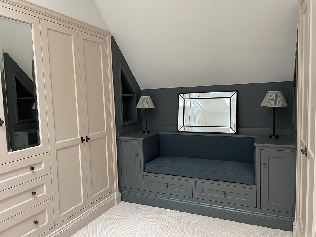 An angled view of the dark green window seat, showing the storage drawers beneath, with the large, mirrored shaker-style wardrobes to the left.